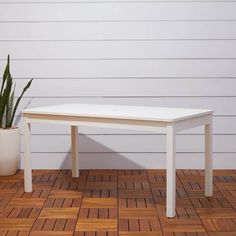 a white table sitting on top of a wooden floor next to a potted plant