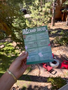 a person holding up a pamphlet in front of a camp site with chairs and trees