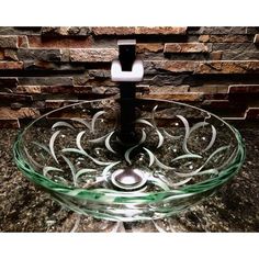 a clear glass bowl with swirl designs on the bottom and a black stand in front of a brick wall