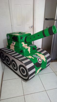 a tank made out of cardboard sitting on top of a tiled floor next to a refrigerator