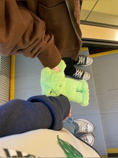 someone is holding a green stuffed animal in their hand while they are sitting on the floor