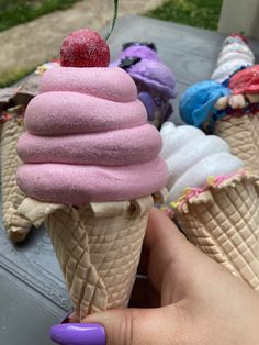 a hand holding an ice cream cone with pink frosting and a cherry on top