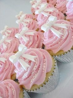 cupcakes with pink frosting and white bows on them are arranged in rows