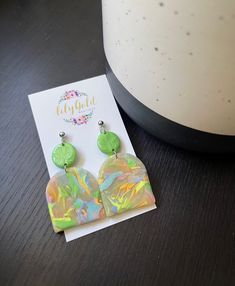 a pair of green earrings sitting on top of a table next to a white card