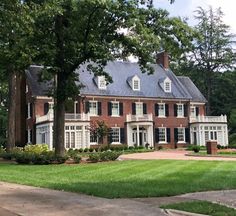 a large red brick house sitting on top of a lush green field next to trees