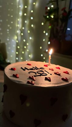 a birthday cake with a lit candle in the middle and some hearts on it's side