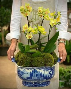 a woman holding a blue and white bowl with flowers in it