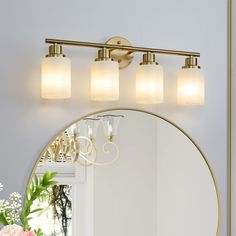 a bathroom vanity with three lights and a mirror on the wall next to flowers in a vase