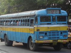 an old blue and yellow bus is driving down the street with people on it's roof