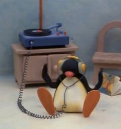 a toy penguin with headphones sitting on the floor next to a record player and chair