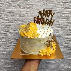 a hand holding a cake with yellow flowers on it and the words happy birthday written on top