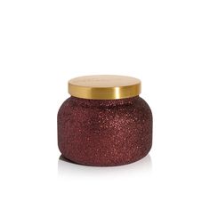 a red candle with a gold lid on a white background, it looks like the inside of a jar