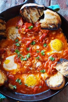 an iron skillet filled with eggs, tomato sauce and bread on top of a wooden table