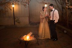 a man and woman standing in front of a fire pit