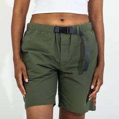 a woman wearing green shorts and a white tank top is standing with her hands in her pockets