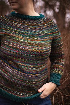 a woman wearing a multicolored sweater in the woods