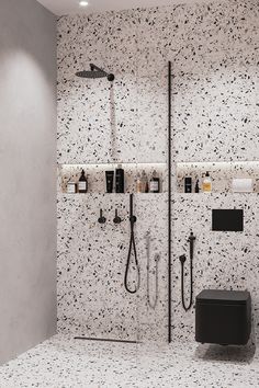 a bathroom with black and white speckles on the walls, shower head, and shelves