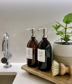 two soap dispensers sitting on a wooden tray next to a potted plant