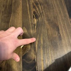 a person's hand is pointing at something on the table that appears to be wood