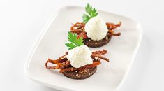 three small appetizers on a white plate topped with sour cream and garnish