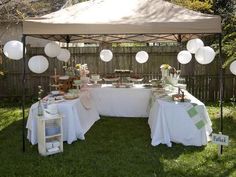 a table set up with plates and desserts under a canopy in the grass near a fence