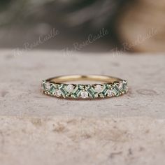 a gold ring with green and white stones on it sitting on a stone slab in front of a rock