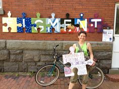 a woman standing next to a bike holding a sign