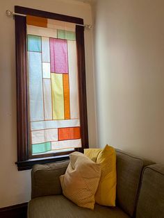 a couch with some pillows on it in front of a stained glass window that is open