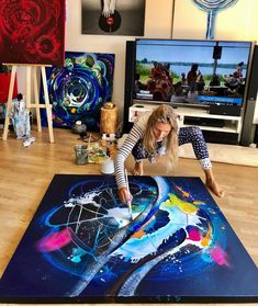 a woman is painting on the floor in front of televisions and other art work