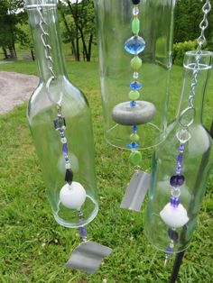 three glass bottles with beads and chains hanging from them on the grass in front of some trees