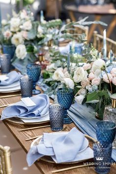 the table is set with blue and white dishes, silver napkins, and floral centerpieces