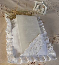 an open book on a lace doily next to a small doll in a box