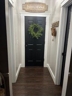 a black front door with a wreath on it and a wooden sign above the door