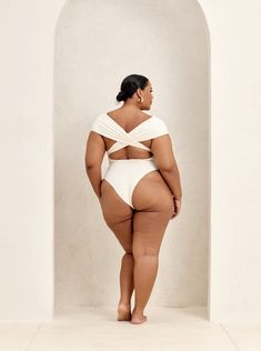 a woman in a white swimsuit standing against a wall with her back to the camera