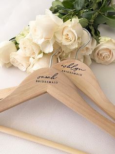 two wooden hangers with names on them next to white roses and flowers in the background