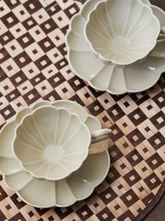 two white dishes sitting on top of a brown and white place mat next to each other