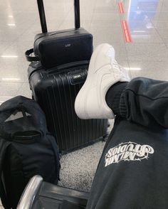 a person's feet resting on luggage in an airport terminal, with their shoes propped up against them