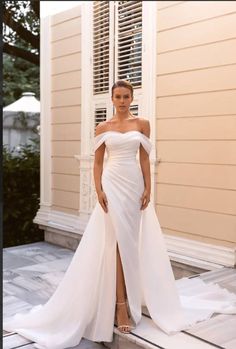 a woman in a white wedding dress standing on a porch next to a house with shutters