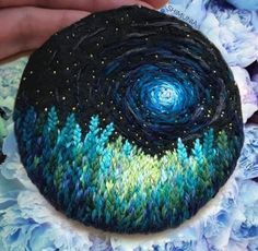 a hand holding a knitted rock with trees and stars in the sky on it