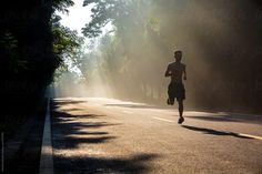 a man running down the middle of a road in the sunbeams with trees on both sides