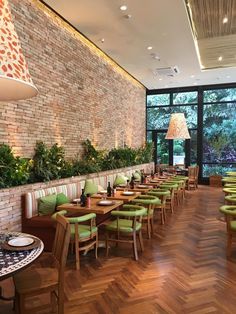 an empty restaurant with green chairs and wooden tables in front of a large brick wall