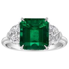 an emerald and diamond ring with three diamonds on the band, set in white gold