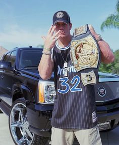 a man standing in front of a truck with his hand up to his face and wearing a wrestling belt