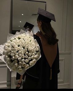 a woman holding a bouquet of white flowers in front of a mirror and wearing a graduation cap