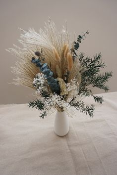 a white vase filled with lots of different types of flowers and plants on top of a table