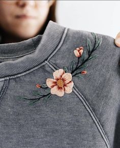 a woman is holding up a sweater with flowers on the front and side of it