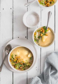 two bowls filled with soup on top of a white wooden table next to spoons