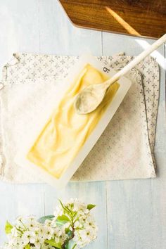 there is a piece of cheese on the table with a spoon next to it and some flowers