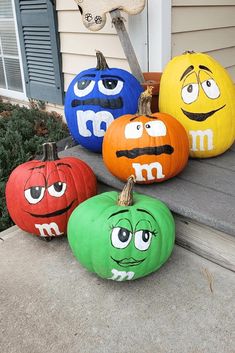 four pumpkins with faces painted on them sitting in front of a house, one is smiling and the other has eyes