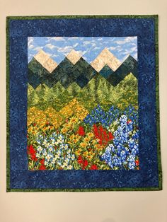 a quilted wall hanging with flowers and mountains in the background